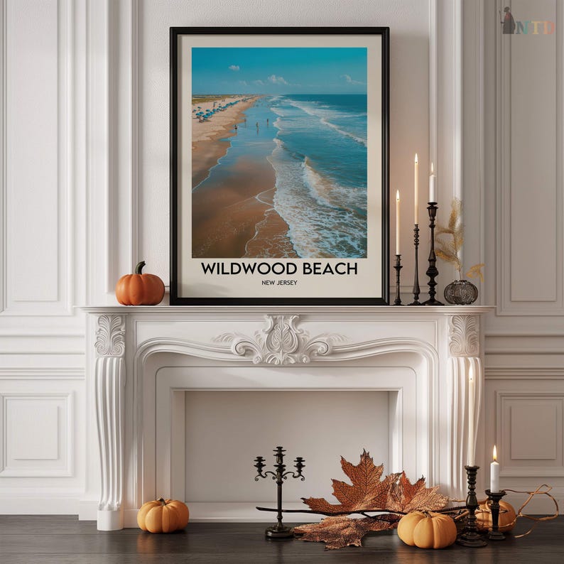 May include: A framed print of Wildwood Beach, New Jersey, showing a coastal scene under a blue sky. The print is displayed on a white mantelpiece, decorated with pumpkins, candles, and autumn leaves. The black frame contrasts with the bright image.