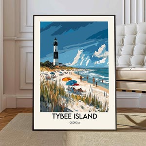May include: A framed art print of Tybee Island, Georgia. The image shows a black and white lighthouse, a sandy beach, and people by the sea. The beach has colourful parasols, and the sky is a mix of blue and white.