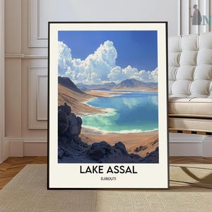 May include: A framed print of a landscape photograph featuring a blue lake surrounded by mountains and a cloudy sky. The text "Lake Assal, Djibouti" is printed below the image.
