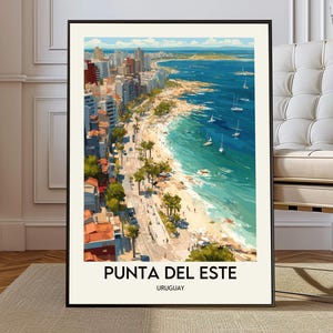 Könnte beinhalten: Ein gerahmter Kunstdruck von Punta del Este, Uruguay. Das Kunstwerk zeigt eine Küstenstadt mit Gebäuden, einem Strand und Segelbooten auf dem Wasser. Der Druck hat einen schwarzen Rahmen und den Text "PUNTA DEL ESTE" und "URUGUAY" unten.