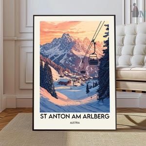 May include: A framed art print of a ski resort scene. The artwork depicts a snowy mountain landscape with a ski lift, cabins, and the text "ST ANTON AM ARLBERG AUSTRIA". The sky is a gradient of orange and pink.