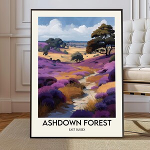 Op de afbeelding: Een ingelijste kunstafdruk van Ashdown Forest, East Sussex. Het landschap toont een pad dat zich een weg baant door velden met paarse en gele bloemen onder een blauwe lucht met witte wolken. Bomen bezaaien de horizon.