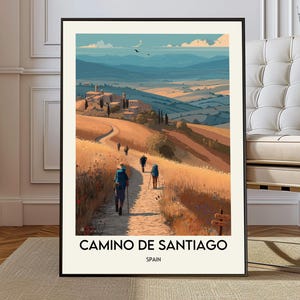 May include: A framed art print depicting the Camino de Santiago in Spain. The artwork shows a path winding through a golden field, with hikers and a distant village. The sky is blue with a few birds. The text "CAMINO DE SANTIAGO" and "SPAIN" are at the bottom.