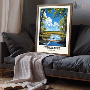 Op de afbeelding: Een vintage poster met een schilderachtig uitzicht op het Everglades National Park. De poster toont een blauwe lucht met witte wolken, weelderige groene bomen en een rustige rivier die door het landschap stroomt. De tekst "Everglades National Park" staat onderaan de poster gedrukt.