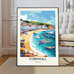 May include: A framed art print of Cornwall, England, featuring a coastal scene with colorful boats, seagulls, and buildings. The artwork has a vibrant color palette of blues, yellows, and oranges, with the word "CORNWALL" at the bottom.