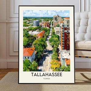 May include: A framed art print of Tallahassee, Florida, featuring a vibrant cityscape. The artwork showcases buildings with red and white facades, lush green trees, and a blue sky. The text "TALLAHASSEE FLORIDA" is displayed at the bottom.