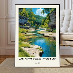 May include: A framed art print of Apple River Canyon State Park in Illinois. The artwork depicts a vibrant river scene with blue water, green trees, and rocky banks under a bright blue sky with fluffy white clouds. The print is in a black frame.