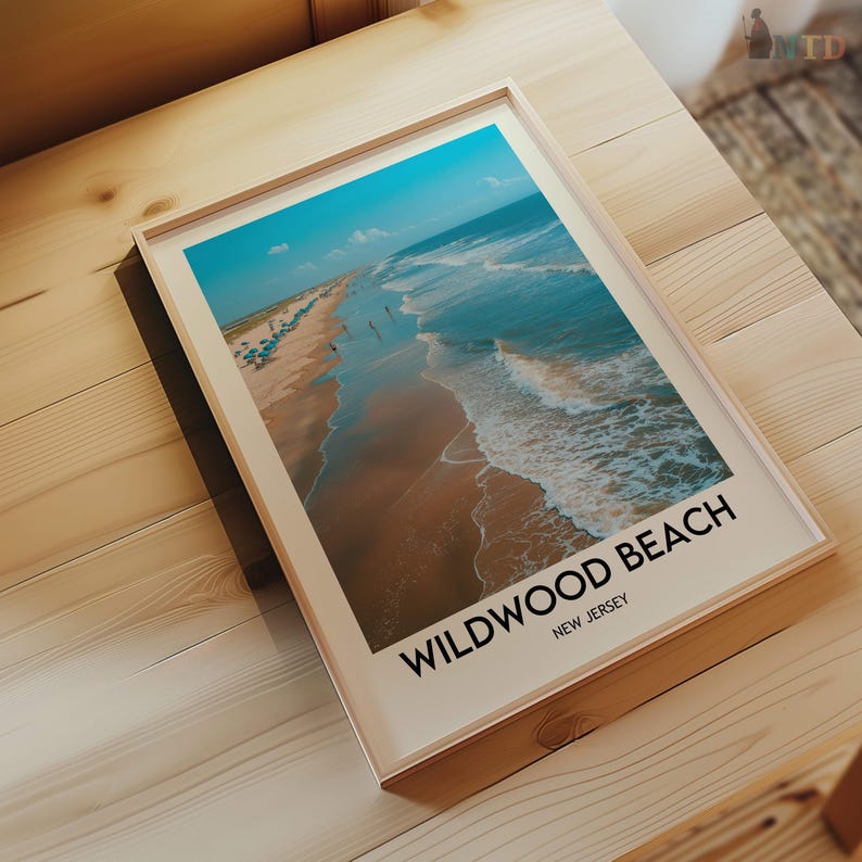 May include: A framed print depicting a beach scene with turquoise water and a sandy shore. The print includes the text "Wildwood Beach, New Jersey" in a bold, black font. The frame is a light wood colour.