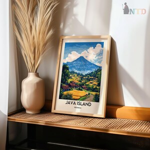May include: A framed art print of Java Island, Indonesia, featuring a vibrant landscape with a blue mountain, green trees, and yellow fields. The print is in a light wood frame and is displayed on a woven shelf next to a beige vase with dried plants.