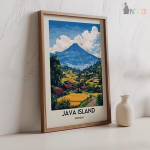 May include: Framed art print of Java Island, Indonesia. The artwork depicts a mountain landscape with a blue sky, white clouds, and a village with yellow fields. The print is in a wooden frame, with the text "JAVA ISLAND" and "INDONESIA".