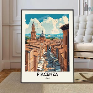May include: A framed art print of Piacenza, Italy, featuring a detailed illustration of a city street scene. The artwork showcases buildings with orange rooftops, a domed structure, and a tall tower under a blue sky with clouds. The word "PIACENZA" is printed at the bottom.