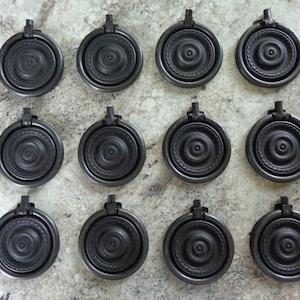 May include: Twelve black metal drawer pulls with a circular design. Each pull has a ring handle and a decorative center.