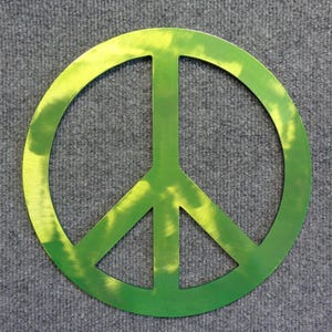 May include: A metallic green peace sign with a brushed finish. The symbol is a circle with a vertical line and two diagonal lines inside. The peace sign is a symbol of peace and non-violence.