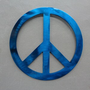 May include: A blue peace sign with a brushed metal finish. The peace symbol is a circle with a vertical line and two diagonal lines inside. The symbol is centered on a gray background.