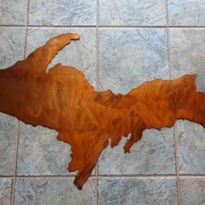 May include: A rusty brown metal cutout of the Upper Peninsula of Michigan. The cutout is on a tiled floor.