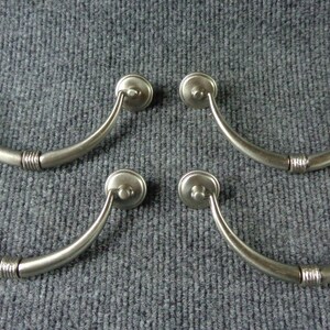 May include: Set of six silver-toned cabinet pulls with a curved, arched design. Each pull has a rounded knob at the top and a smooth, polished finish.