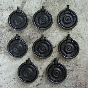 May include: Nine black metal cabinet knobs with a ring pull and a decorative design. The knobs have a circular shape with a raised center and a textured outer ring.