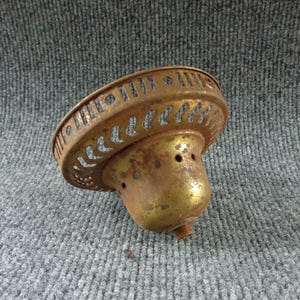 May include: A vintage brass lamp canopy with a weathered patina and signs of oxidation. The circular fixture features a decorative perforated rim with a repeating pattern of vertical slots and small circular cutouts, and a central threaded stem.