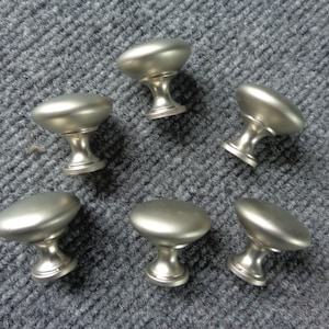 May include: Six silver cabinet knobs with a round, slightly domed top and a short, cylindrical base.