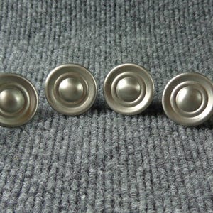 May include: Six silver-toned round cabinet knobs with a raised center and a decorative rim.