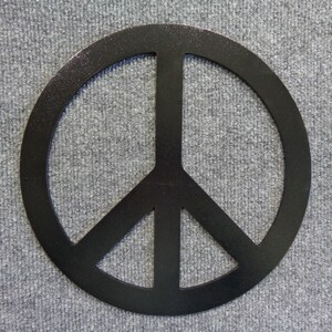 May include: A black peace sign, a symbol of peace and non-violence, is centered against a gray textured background. The peace symbol is a circle with three downward-pointing lines.