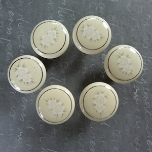 May include: Six cream-colored ceramic cabinet knobs with a gold trim and a floral design.