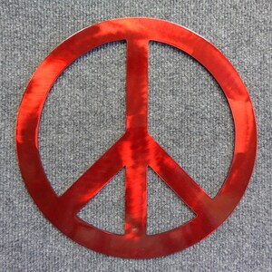 May include: A red peace sign made of metal. The peace symbol is a circle with a vertical line through the center and two diagonal lines extending downward. The sign is a bright, shiny red color.
