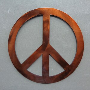 May include: A copper-colored peace sign, a symbol of peace and harmony. The sign is made of metal and has a rustic, weathered appearance. The peace symbol is a popular design element for home decor and accessories.
