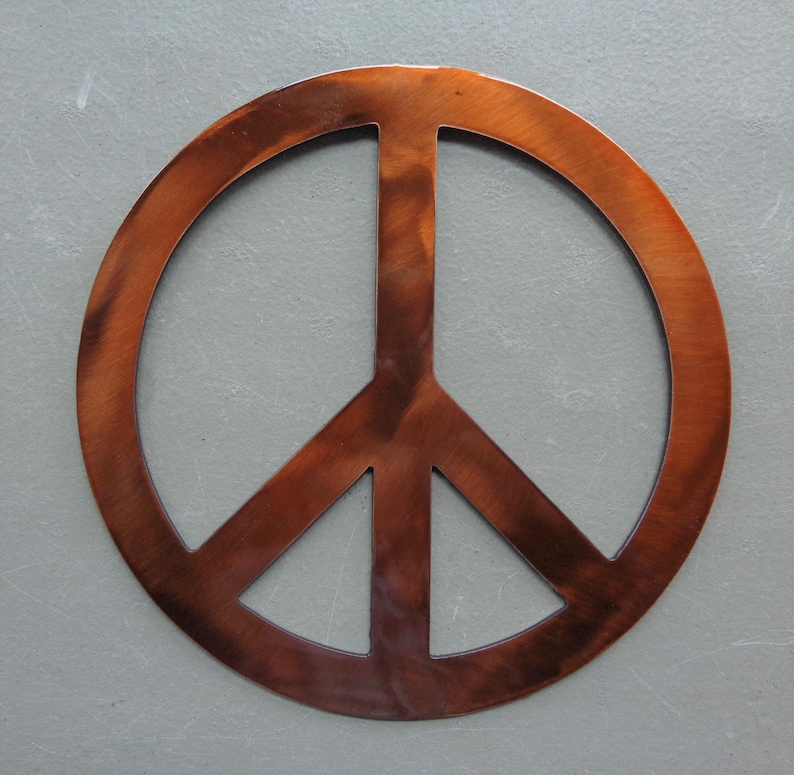 May include: A copper-colored peace sign, a symbol of peace and harmony. The sign is made of metal and has a rustic, weathered appearance. The peace symbol is a popular design element for home decor and accessories.