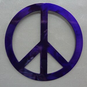 May include: A vibrant, deep purple peace sign. The symbol is a circle with a vertical line and two diagonal lines inside. The color has a marbled effect, with lighter shades of purple throughout. The background is a light gray.