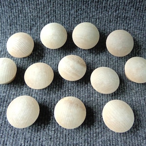 May include: A collection of 12 natural wood round knobs. The knobs are smooth and have a light brown color.