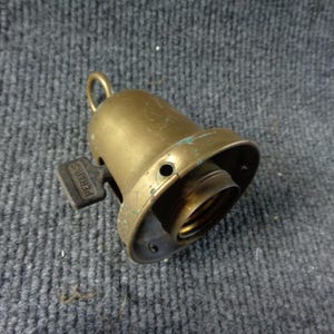 May include: A vintage brass light socket featuring a bell-shaped housing with a small hanging loop at the top. A dark-colored turn-key switch is attached to the side, clearly embossed with the brand name PERKINS. The metal shows signs of age.