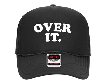 May include: Black trucker hat with the words "OVER IT." in bold white letters. The hat has a mesh back and a curved brim. A small tag on the front brim reads "OTTO" and "Trucker".