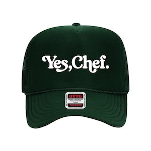May include: A dark green trucker hat with the text "Yes, Chef" in white script across the front. The hat has a mesh back and a curved brim. A small white tag is visible on the front.