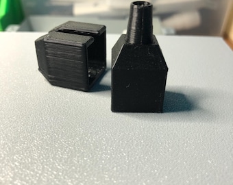 May include: Two black 3D printed plastic pieces, one is a hollow square with a small opening on one side, the other is a solid piece with a small opening on the top.