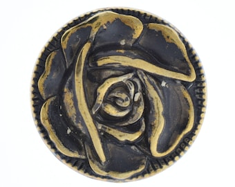 May include: A gold-colored metal button with a black rose design. The button has a raised, textured design and a circular shape.