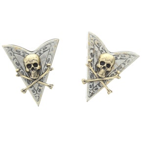 May include: A pair of silver and gold earrings shaped like arrowheads with a skull and crossbones design.