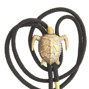 May include: A black bolo tie with a gold-toned turtle pendant. The turtle is detailed with a textured shell and has a raised head and legs.