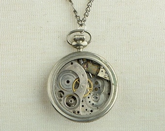 May include: A silver chain necklace with a silver pocket watch pendant. The watch face is open, revealing the inner workings of the watch.