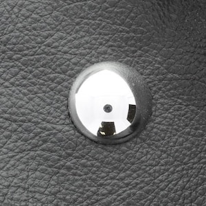 May include: Close-up of a black leather surface with a silver metal button.