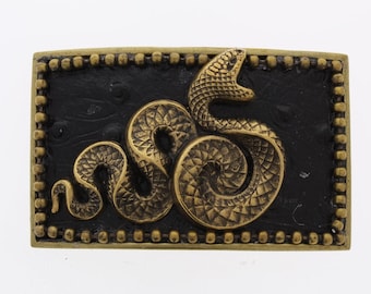 Peut inclure: Une boucle de ceinture dorée avec un fond noir et un motif de serpent en relief.