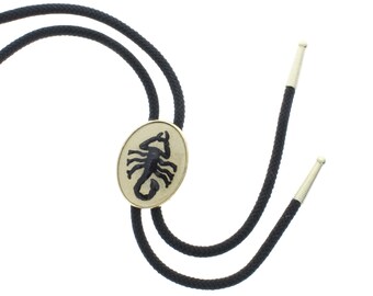 Può includere: Cravatta bolo nera con un pendente ovale dorato con un design a scorpione nero.