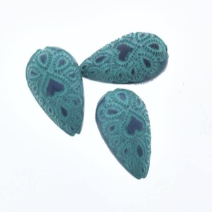 Puede incluir: Tres cuentas de vidrio azul turquesa con un patrón de encaje decorativo. Las cuentas tienen forma de lágrima y un centro azul oscuro.