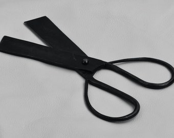 Puede incluir: Tijeras de metal negro con un solo remache en el centro de las cuchillas. Las tijeras tienen un diseño simple y están hechas de una sola pieza de metal.