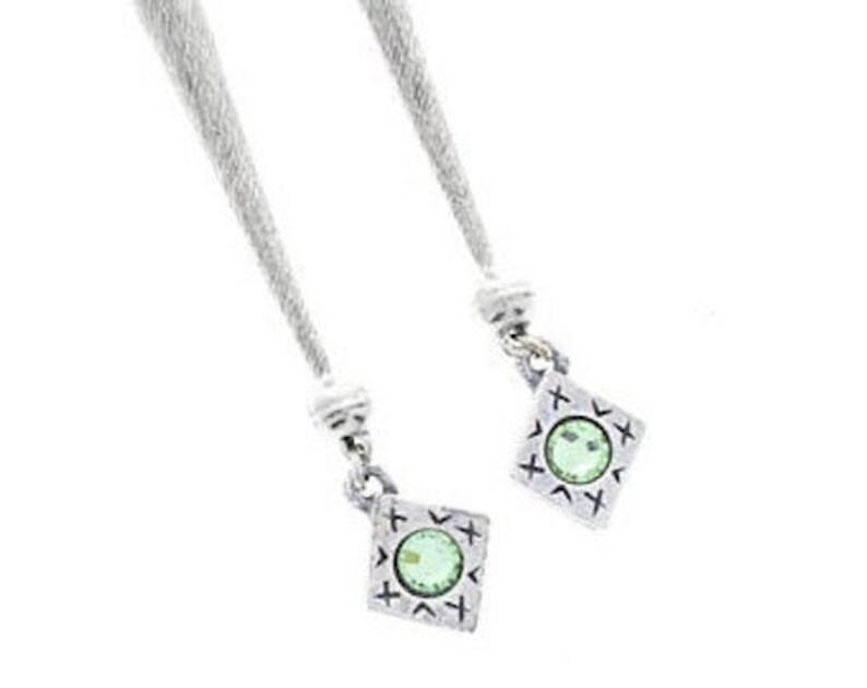 Puede incluir: Dos colgantes de plata con una piedra preciosa verde en el centro de cada uno. Los colgantes tienen forma de diamante con un patr&oacute;n decorativo alrededor de los bordes.
