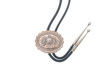 May include: A silver bolo tie with a black cord and a decorative oval pendant featuring a stylized bird design.