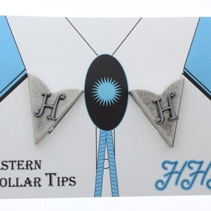 May include: A pair of silver Western collar tips with the letter "H" on each. The tips are displayed on a white card with a blue background and the text "WESTERN COLLAR TIPS" and "HJHJ".