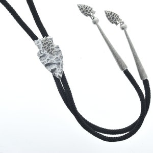 Puede incluir: Un corbatín negro con puntas de flecha plateadas. Las puntas de flecha tienen una superficie texturizada.