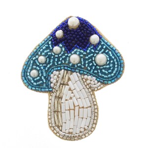 May include: A beaded mushroom-shaped brooch with a blue and white color scheme. The mushroom cap is a mix of dark and light blue beads, with white pearl-like beads. The stem is made of white and silver beads, and the edges are outlined in gold.