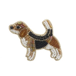 May include: A beaded dog pin in a standing pose. The dog has a brown and black body with white and gold accents. The pin is made with small beads and has a gold-colored outline.